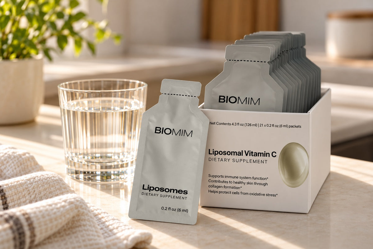 Biomim REVIVE Liposomal Vitamin C liquid packets in an open box beside a glass of water.